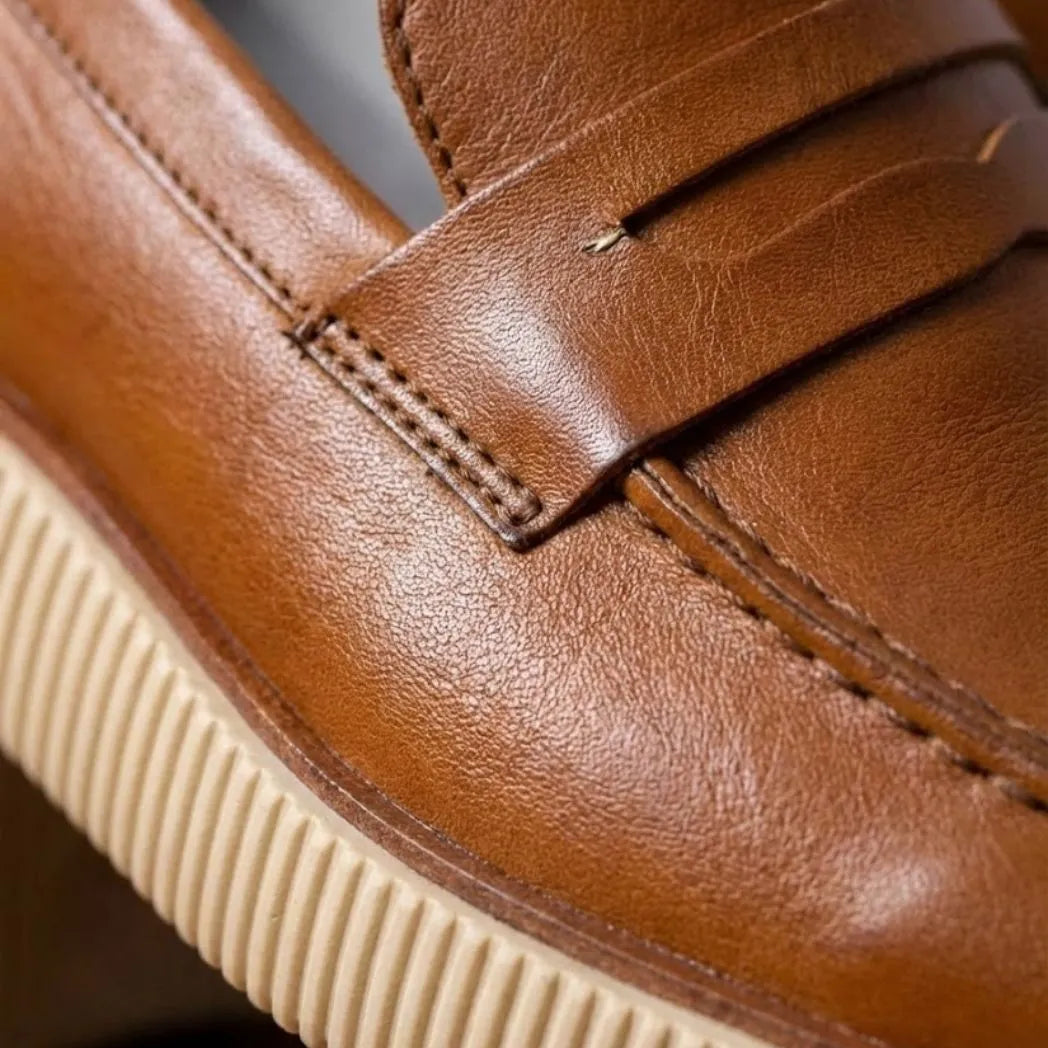 Mocassim Loafer Londres de Couro: detalhe da superfície marrom, da faixa frontal e da sola bege de borda estriada.
