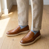 Mocassim Loafer Londres de Couro: par marrom com sola bege usado com calça clara e meias cinza.