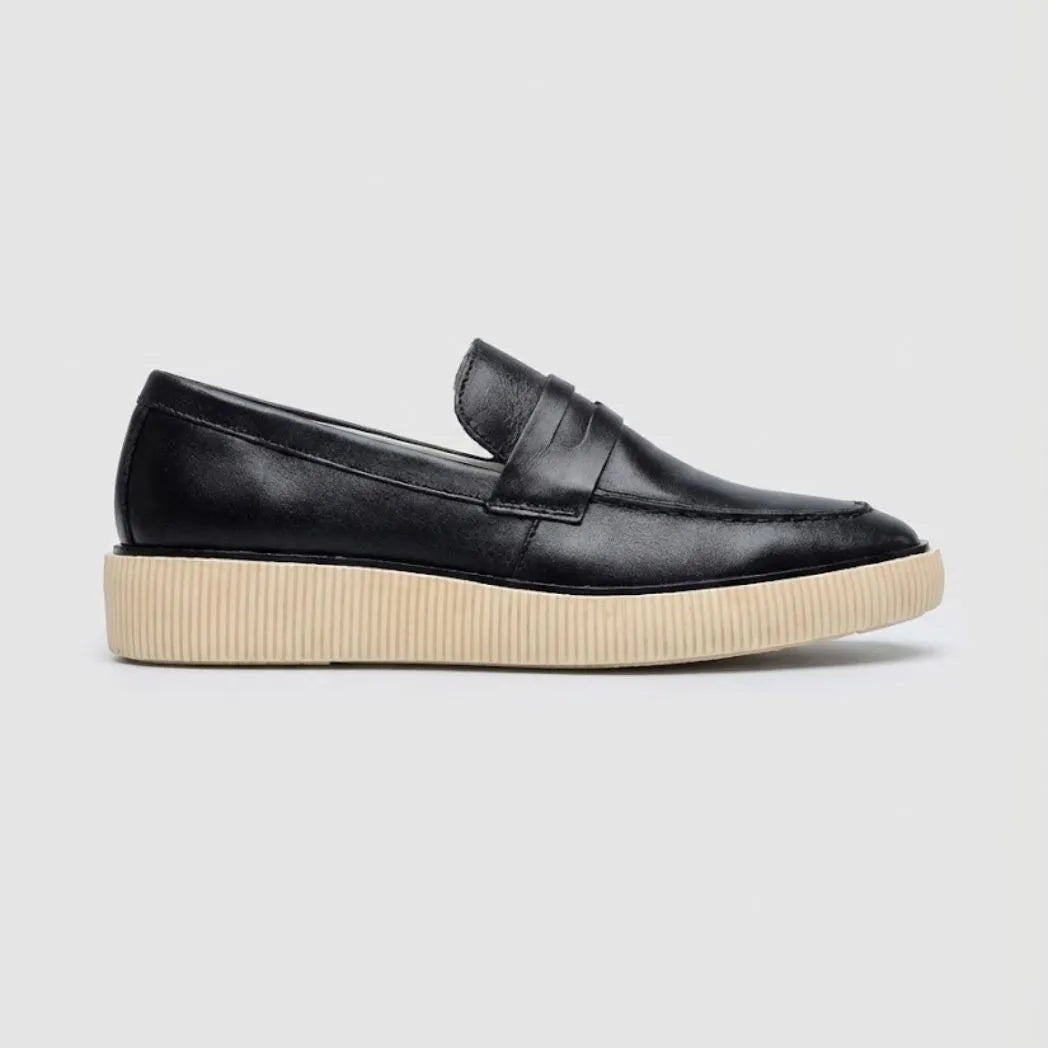 Mocassim Loafer Urban Londres de Couro: modelo preto de perfil, com faixa frontal e sola bege de borda estriada.