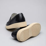 Mocassim Loafer Urban Londres de Couro: par preto com um sapato virado, mostrando a sola bege com sulcos.