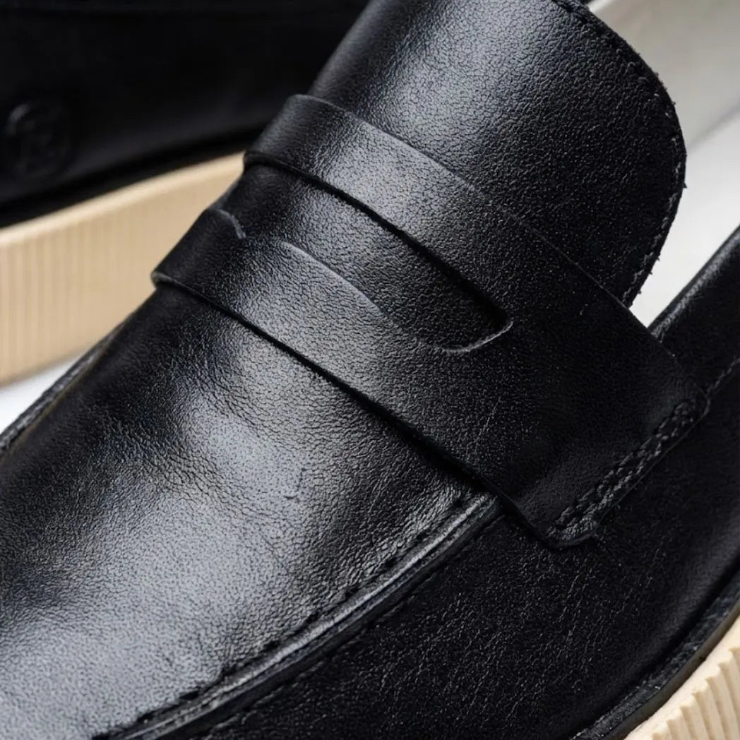 Mocassim Loafer Urban Londres de Couro: detalhe da superfície preta, da faixa frontal e da borda da sola bege.