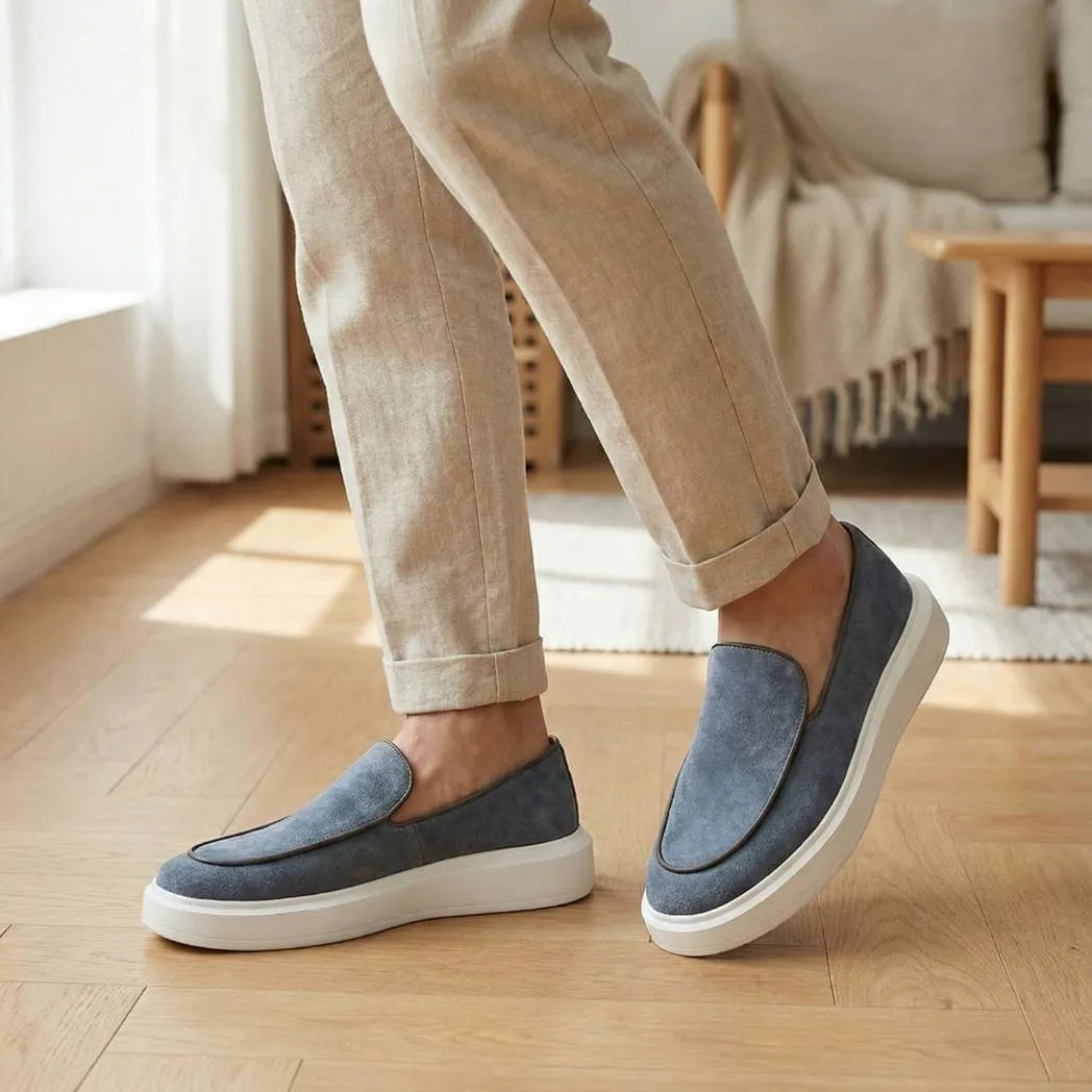 Mocassim Loafer de Camurça Vanguard: par cinza com sola branca usado com calça clara dobrada na barra.