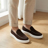 Mocassim Loafer de Camurça Vanguard: par marrom-escuro com sola branca usado com calça bege dobrada na barra.