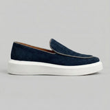 Mocassim Loafer de Camurça Vanguard: modelo azul-escuro de perfil, com contorno claro na parte frontal e sola branca.