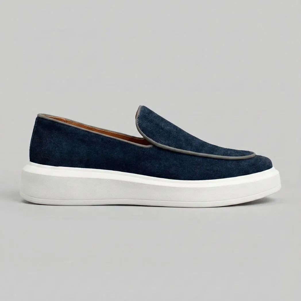 Mocassim Loafer de Camurça Vanguard: modelo azul-escuro de perfil, com contorno claro na parte frontal e sola branca.