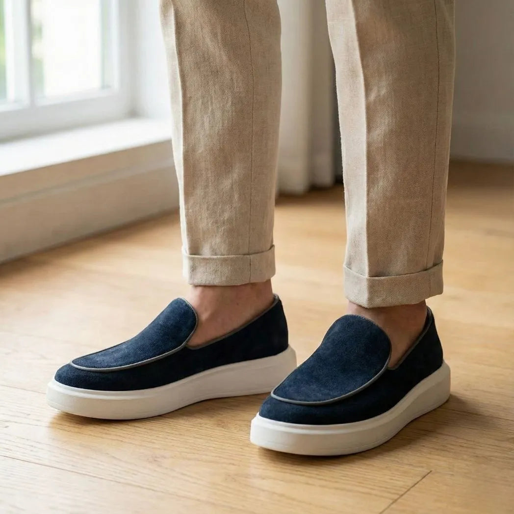 Mocassim Loafer de Camurça Vanguard: par azul-escuro com sola branca usado com calça clara dobrada na barra.