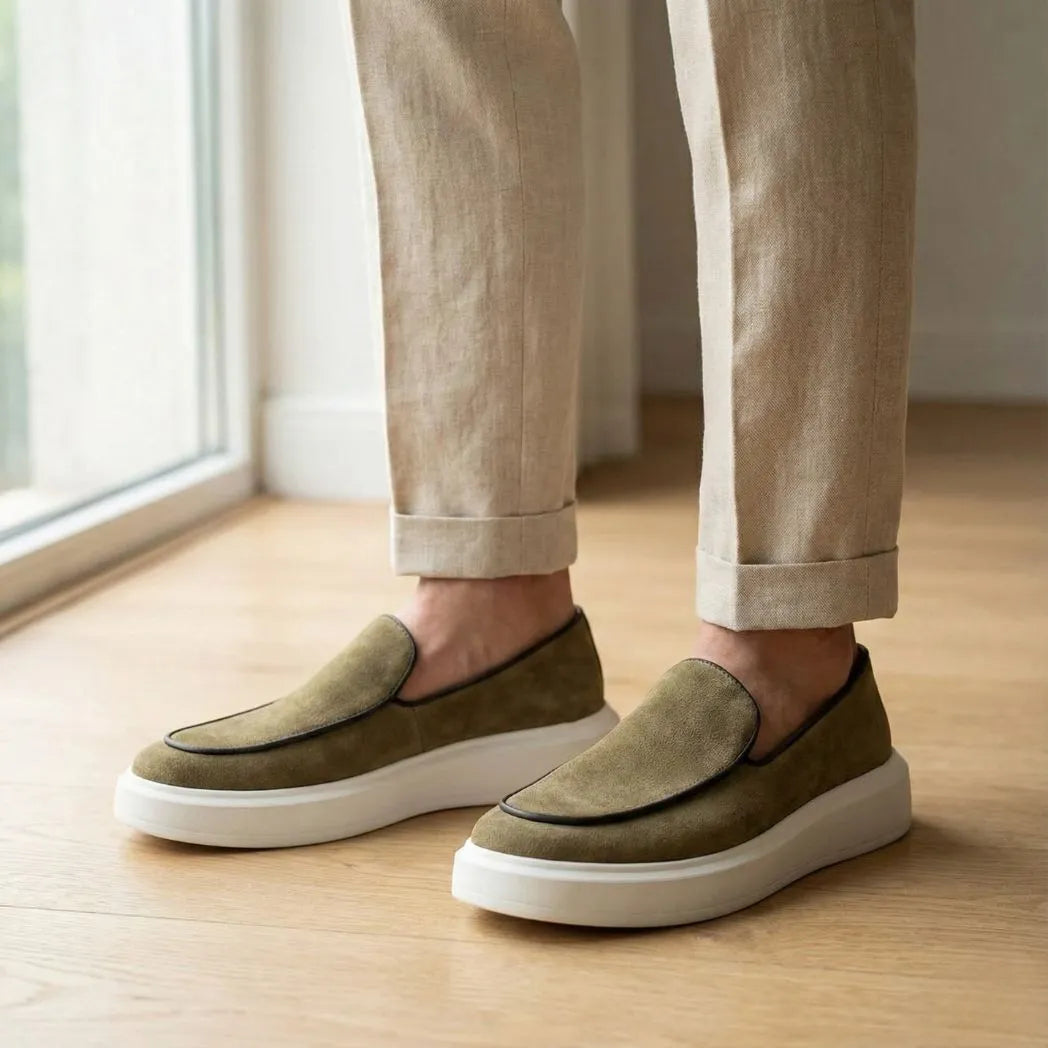 Mocassim Loafer de Camurça Vanguard: par verde-oliva com sola branca usado com calça clara dobrada na barra.