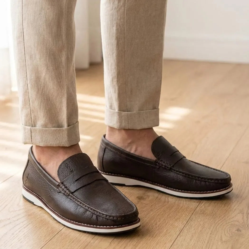Mocassim Loafer de Couro Berlin Edição Limitada X-20: par marrom-escuro com borda branca na sola usado com calça clara dobrada na barra.