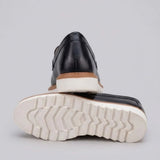 Mocassim Loafer de Couro Napoli: par preto com um sapato virado, mostrando a sola branca com sulcos profundos.