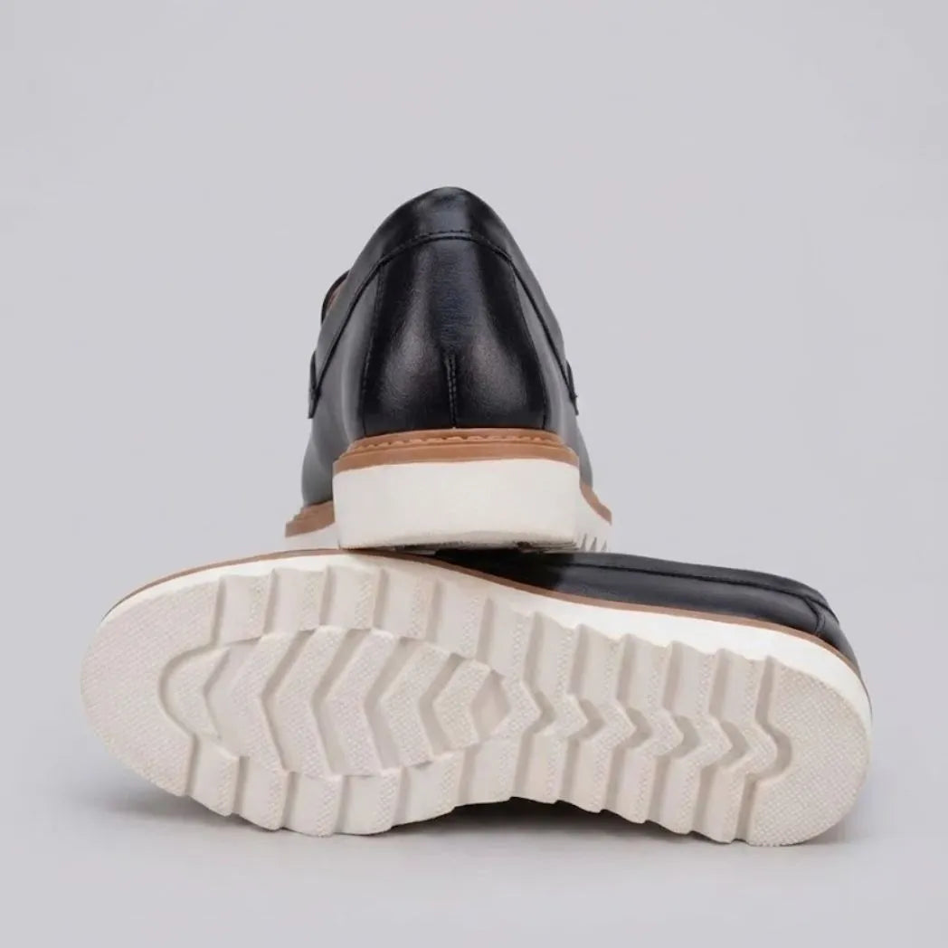 Mocassim Loafer de Couro Napoli: par preto com um sapato virado, mostrando a sola branca com sulcos profundos.