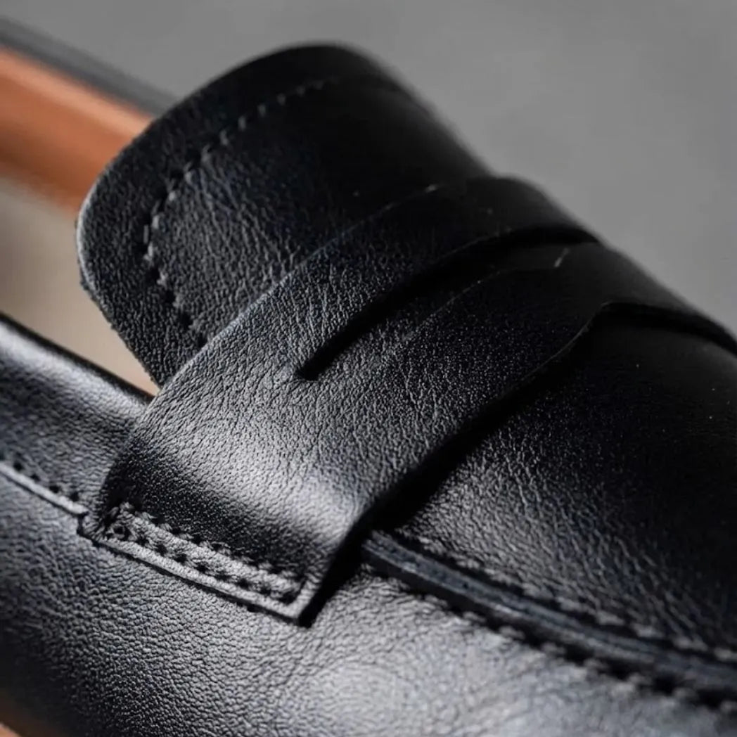 Mocassim Loafer de Couro Napoli: detalhe da superfície preta, da faixa frontal e da costura.