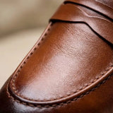 Mocassim Loafer de Couro Napoli: detalhe da superfície marrom e da costura no contorno da parte frontal.
