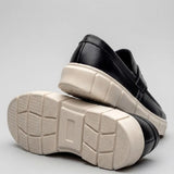 Par do modelo Mocassim Lunar Tratorado, na cor preto, com um dos solados voltado para a câmera.