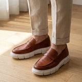 Mocassim Lunar Tratorado na cor marrom, usado com calça clara de barra dobrada.