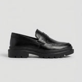 Mocassim Masculino Costurado Piettro: modelo preto de perfil, com faixa frontal e sola preta de sulcos largos.