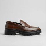 Mocassim Masculino Costurado Piettro: modelo marrom-escuro de perfil, com faixa frontal e sola preta de sulcos profundos.