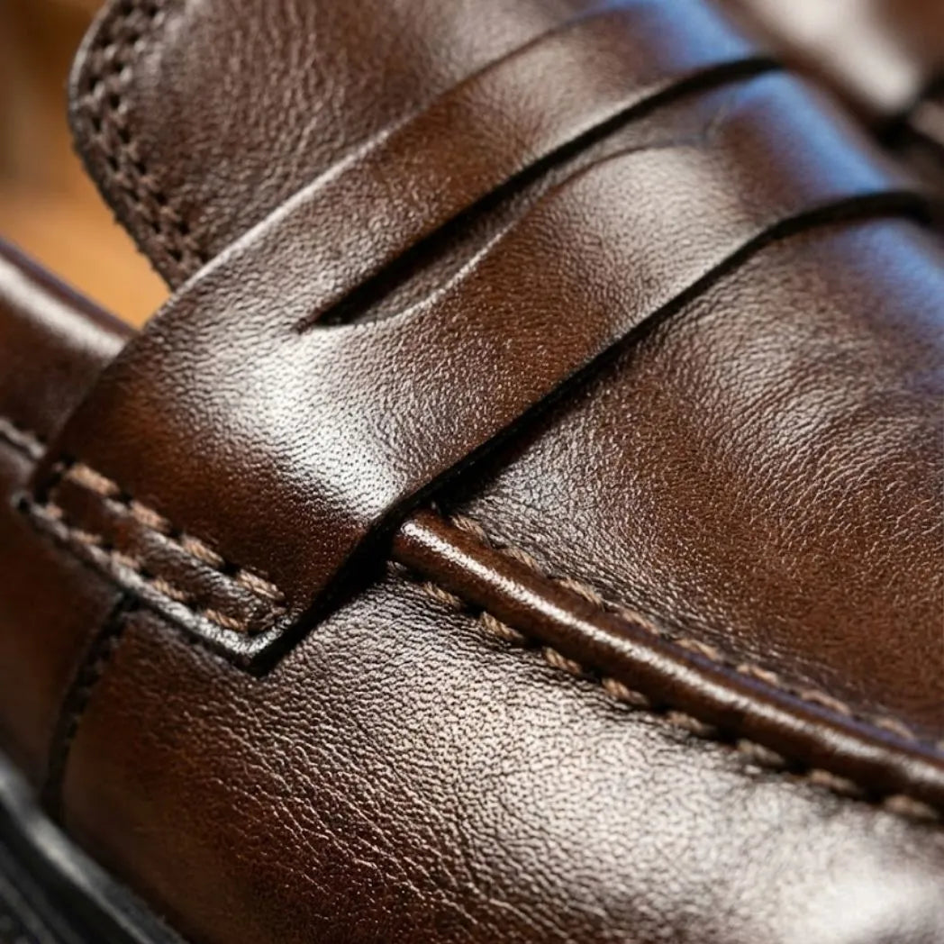 Mocassim Masculino Costurado Piettro: detalhe da superfície marrom-escura, da faixa frontal e da costura.