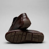 Mocassim Masculino Driver de Couro: par marrom-escuro com um sapato virado, mostrando a sola marrom com sulcos.
