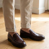 Mocassim Masculino Genova Loafer Couro: par marrom-escuro usado com calça bege dobrada na barra.