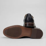 Mocassim Masculino Paris Loafer de Couro: par preto com um sapato virado, mostrando a sola marrom.