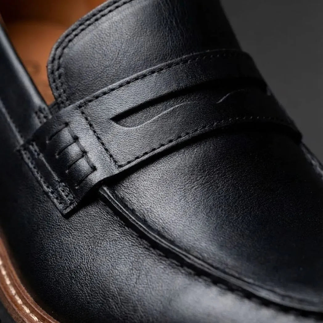 Mocassim Masculino Siena Loafer de Couro: detalhe da superfície preta, da faixa frontal e da costura.