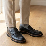 Mocassim Masculino Siena Loafer de Couro: par preto com borda marrom na sola usado com calça clara dobrada na barra.