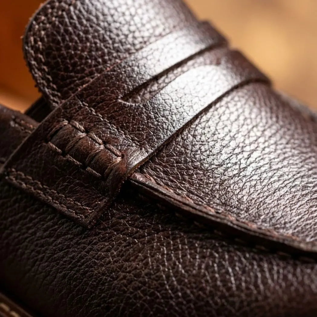 Mocassim Masculino Siena Loafer de Couro: detalhe da textura marrom-escura, da faixa frontal e da costura.