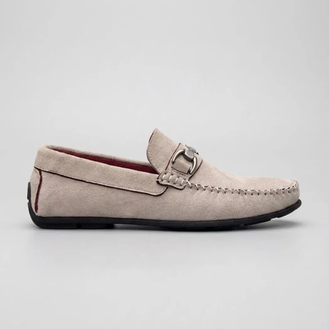 Mocassim Milano Driver com Fivela: modelo claro de perfil, com ferragem retangular prateada, costura frontal e sola preta.