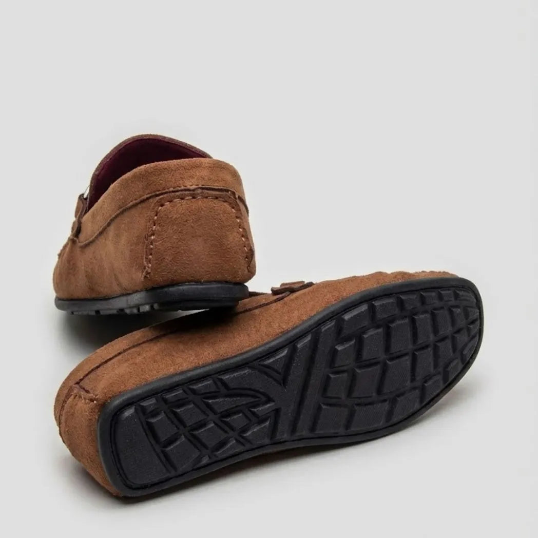 Par do modelo Mocassim Milano Driver com Fivela, na cor marrom, com um dos solados voltado para a câmera.