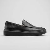 Mocassim Minimalista de Couro: modelo preto de perfil, com parte frontal sem faixa e sola preta.