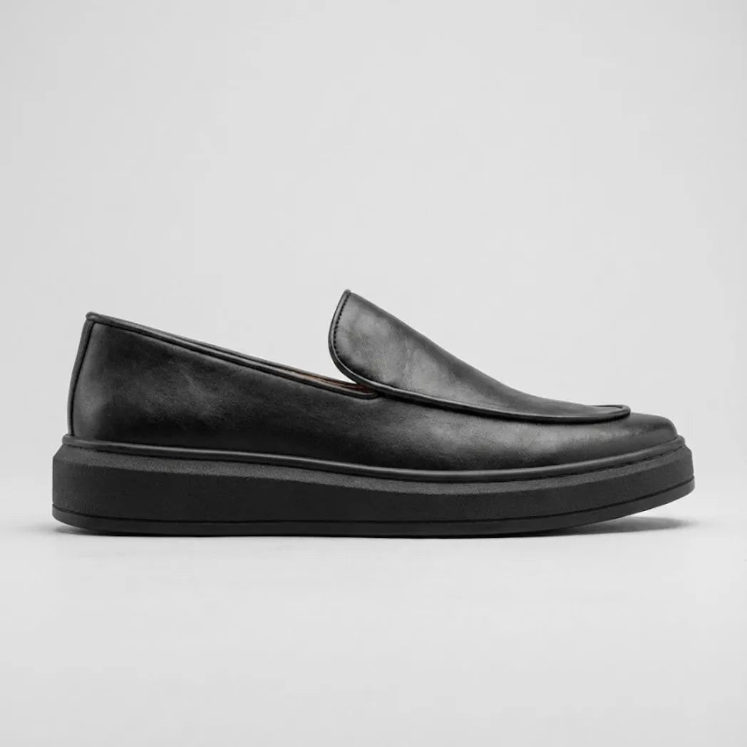 Mocassim Minimalista de Couro: modelo preto de perfil, com parte frontal sem faixa e sola preta.