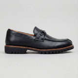 Mocassim Napoli com Fivela: modelo preto de perfil, com pequena ferragem frontal, borda marrom e sola preta com sulcos.
