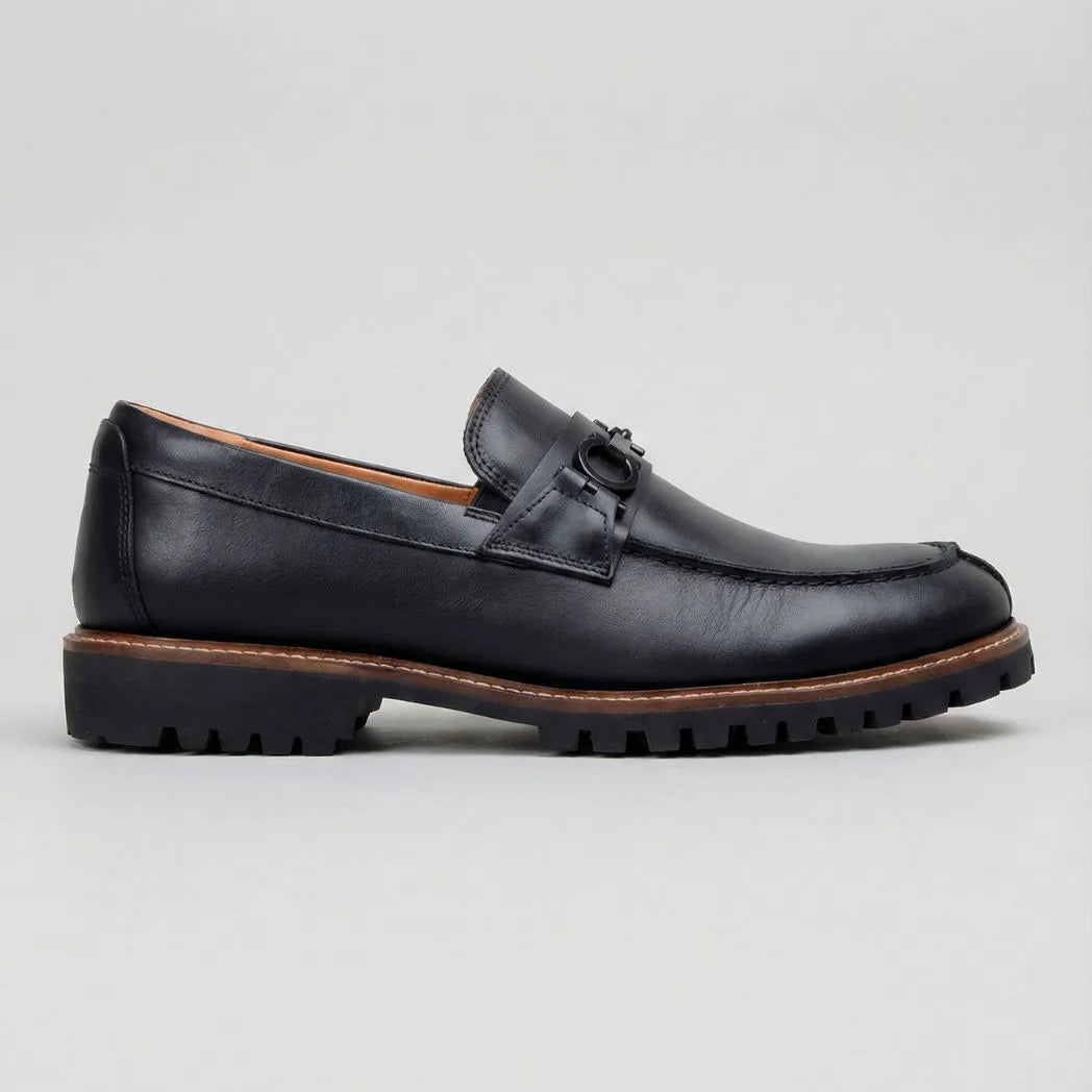 Mocassim Napoli com Fivela: modelo preto de perfil, com pequena ferragem frontal, borda marrom e sola preta com sulcos.
