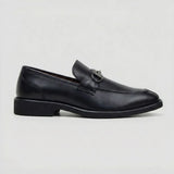 Mocassim Nero Rebel com Fivela: modelo preto de perfil, com ferragem frontal escura e salto baixo preto.