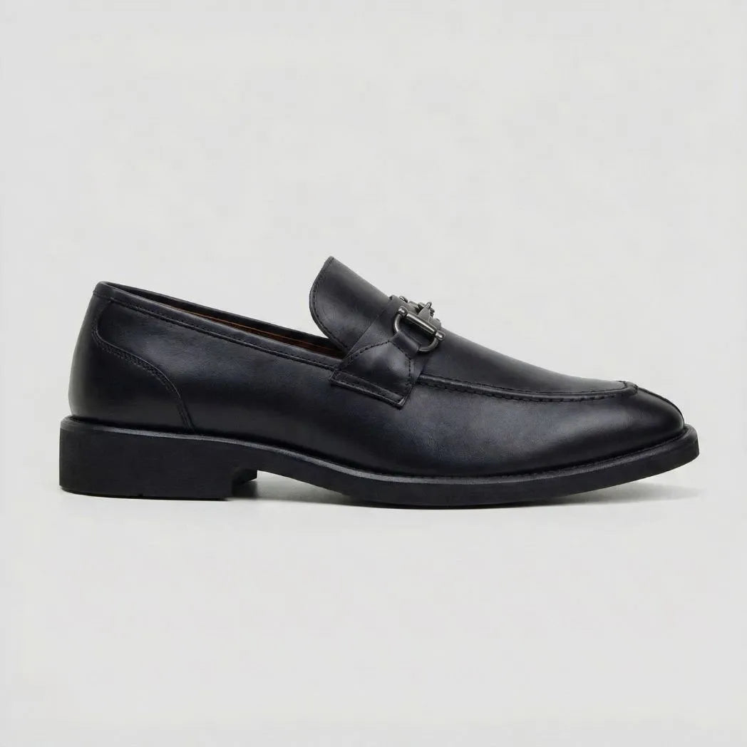 Mocassim Nero Rebel com Fivela: modelo preto de perfil, com ferragem frontal escura e salto baixo preto.