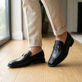 Mocassim Nero Rebel com Fivela na cor preto, usado com calça clara de barra dobrada.