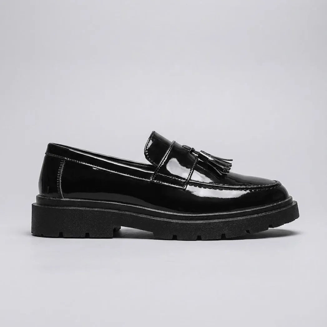 Mocassim Obsidian de Couro: modelo preto brilhante de perfil, com enfeites de franjas e sola preta de sulcos profundos.