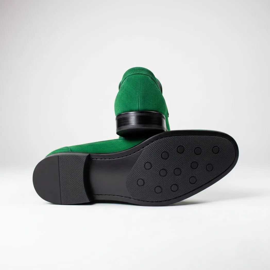 Par do modelo Mocassim Penny Loafer Milano Cognac, na cor verde, com um dos solados voltado para a câmera.