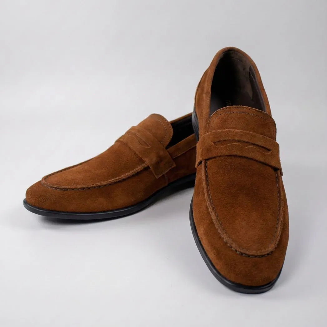 Mocassim Penny Loafer Milano Cognac: par marrom em posição cruzada, com faixa frontal e sola preta.