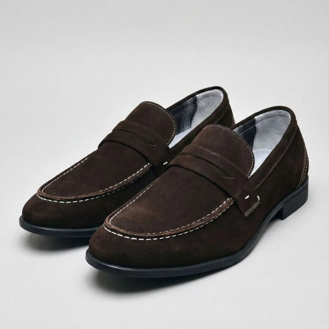 Mocassim Penny Loafer Milano Cognac: par marrom-escuro em vista diagonal, com faixa frontal e costura clara.