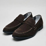 Mocassim Penny Loafer Milano Cognac: par marrom-escuro em vista diagonal, com faixa frontal e costura clara.