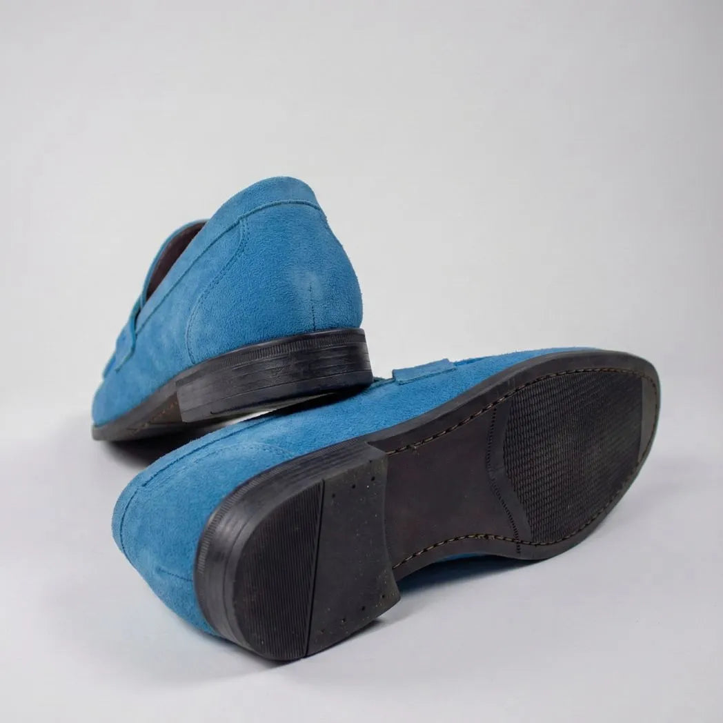 Mocassim Penny Loafer Milano Cognac: par azul com um sapato virado, mostrando a sola preta.