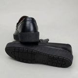 Par do modelo Mocassim Plataform com Fivela, na cor preto, com um dos solados voltado para a câmera.