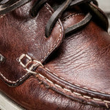 Mocassim Sider de Couro: detalhe da superfície marrom, dos cadarços e da costura clara na parte frontal.