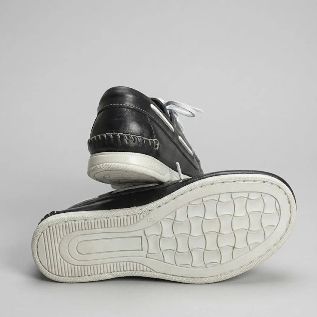 Mocassim Sider de Couro: par preto com um sapato virado, mostrando a sola clara com relevo.