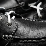Mocassim Sider de Couro: detalhe da superfície preta, dos cadarços brancos, dos ilhós e da costura frontal.