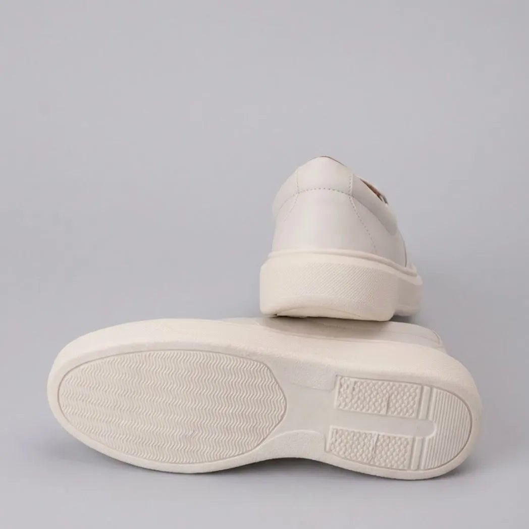 Mocassim Slip On Casual de Couro: par branco com um sapato virado, mostrando a sola clara com sulcos.