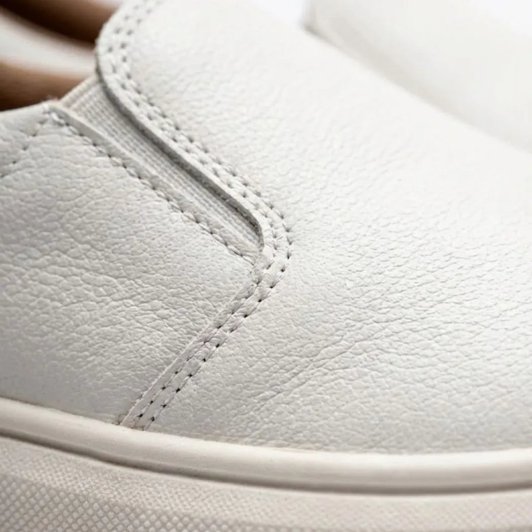 Mocassim Slip On Casual de Couro: detalhe da textura branca, da costura lateral e da borda da sola clara.