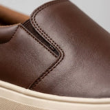 Mocassim Slip On Casual de Couro: detalhe da superfície marrom, da costura lateral e da borda da sola bege.