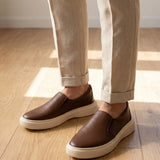 Mocassim Slip On Casual de Couro: par marrom com sola bege usado com calça clara dobrada na barra.